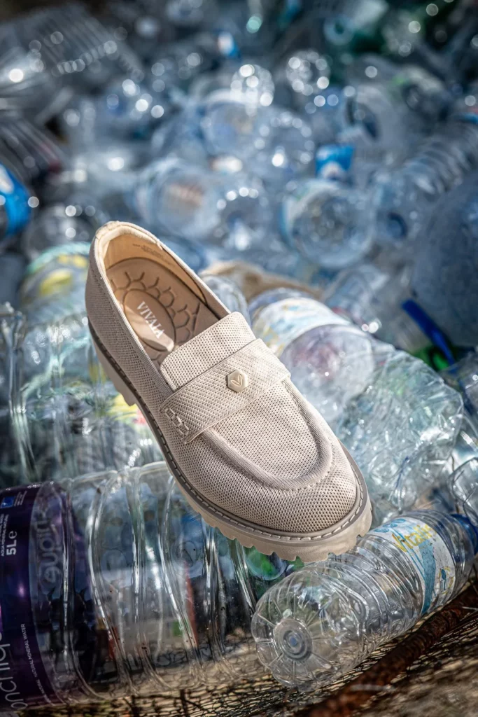 Un mocassin beige de la marque VIVAIA est posé sur un tas de bouteilles en plastique vides, en extérieur sous la lumière du jour.