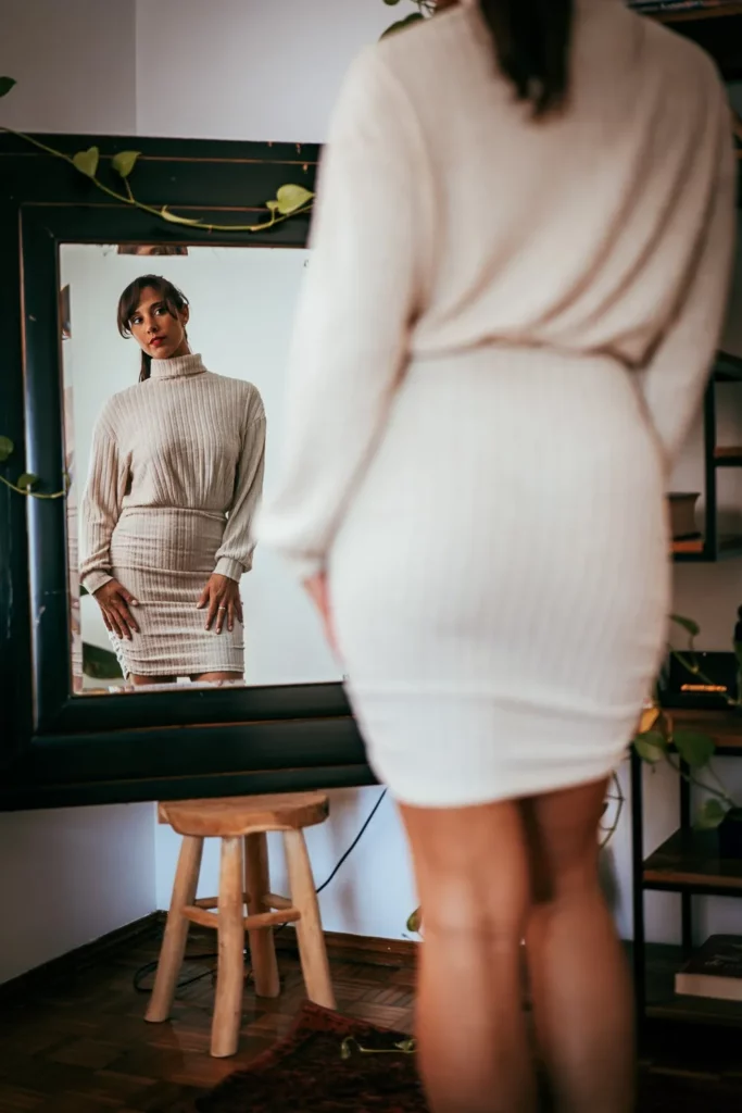 Caroline essaie une robe beige côtelée devant un miroir dans une pièce décorée de plantes et de mobilier en bois à Tavira, Algarve, en novembre 2024.