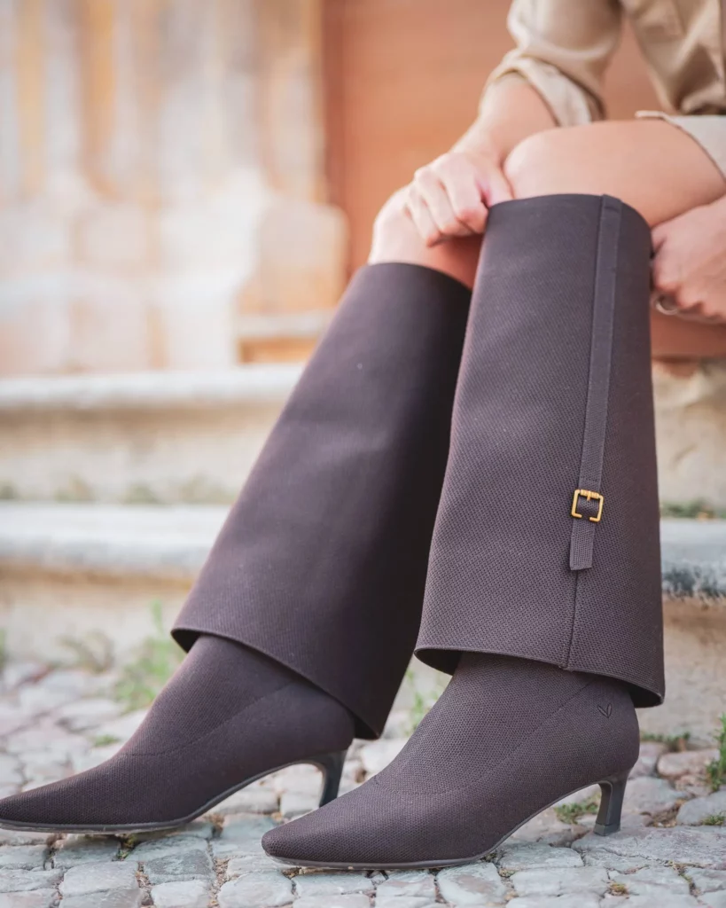 Gros plan sur les jambes de Caroline portant des bottes marron à talons sur un sol pavé, devant un escalier en pierre à Tavira en Algarve, en février 2025.
